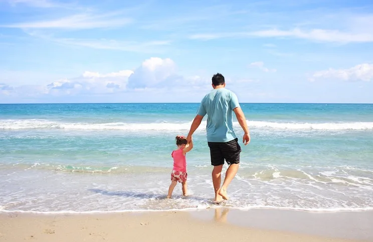 A father and daughter walking into the sea at a Barcelona beach
